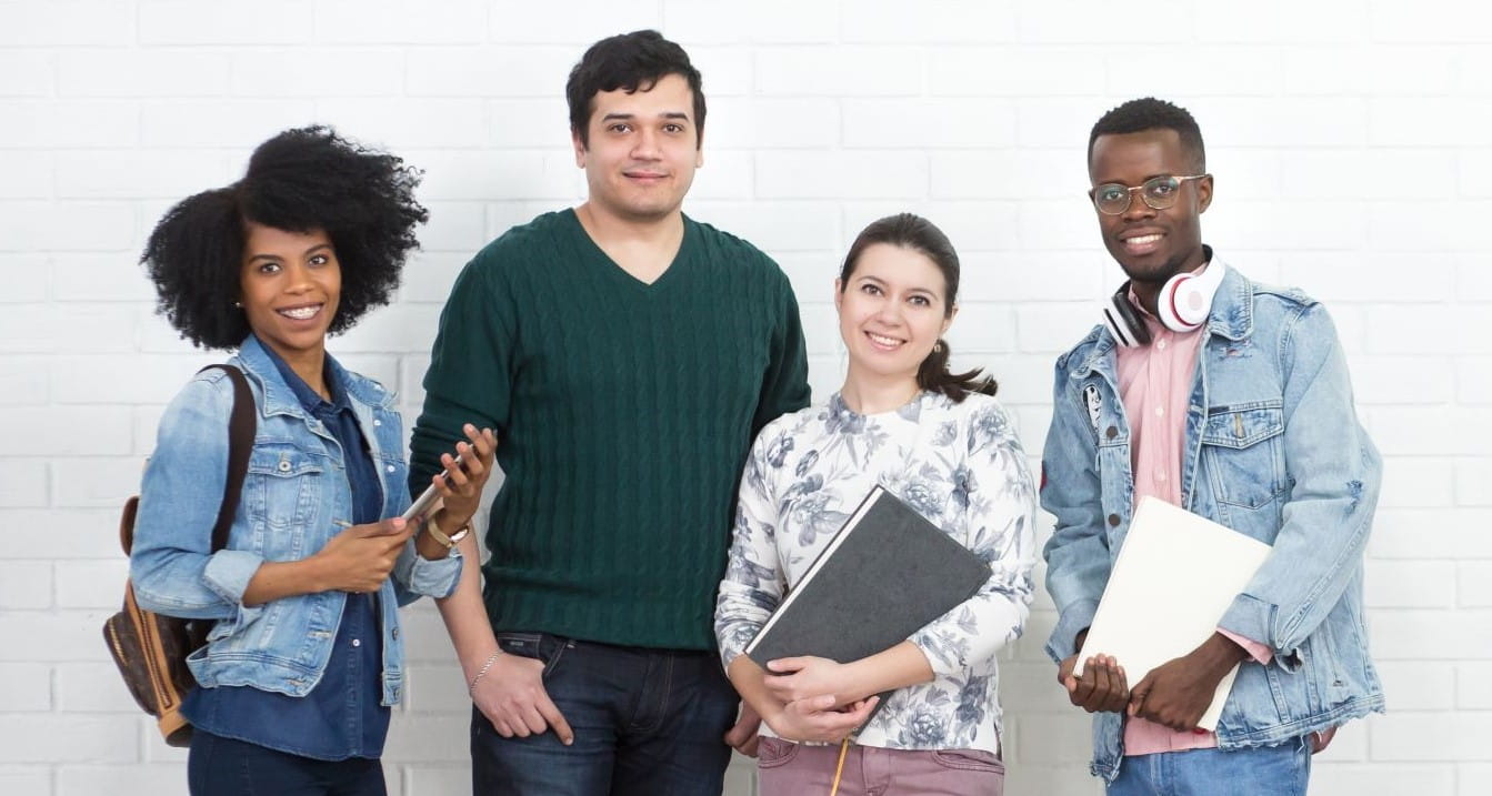 Happy college students with books standing in front of a brick wall