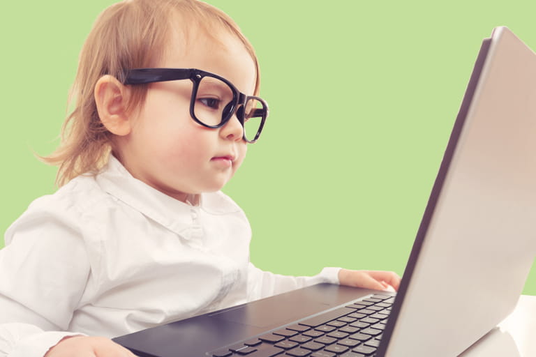 Photo of a toddler wearing glasses looking at a laptop