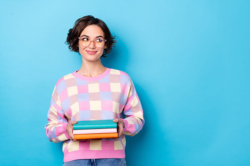 Photo of young adult female student holding books, isolated on blue background