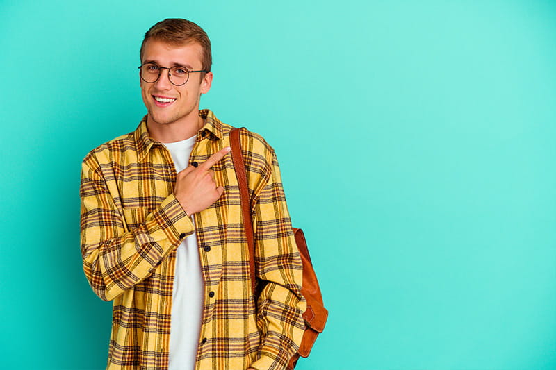 Young male student with bookbag isolated on blue background