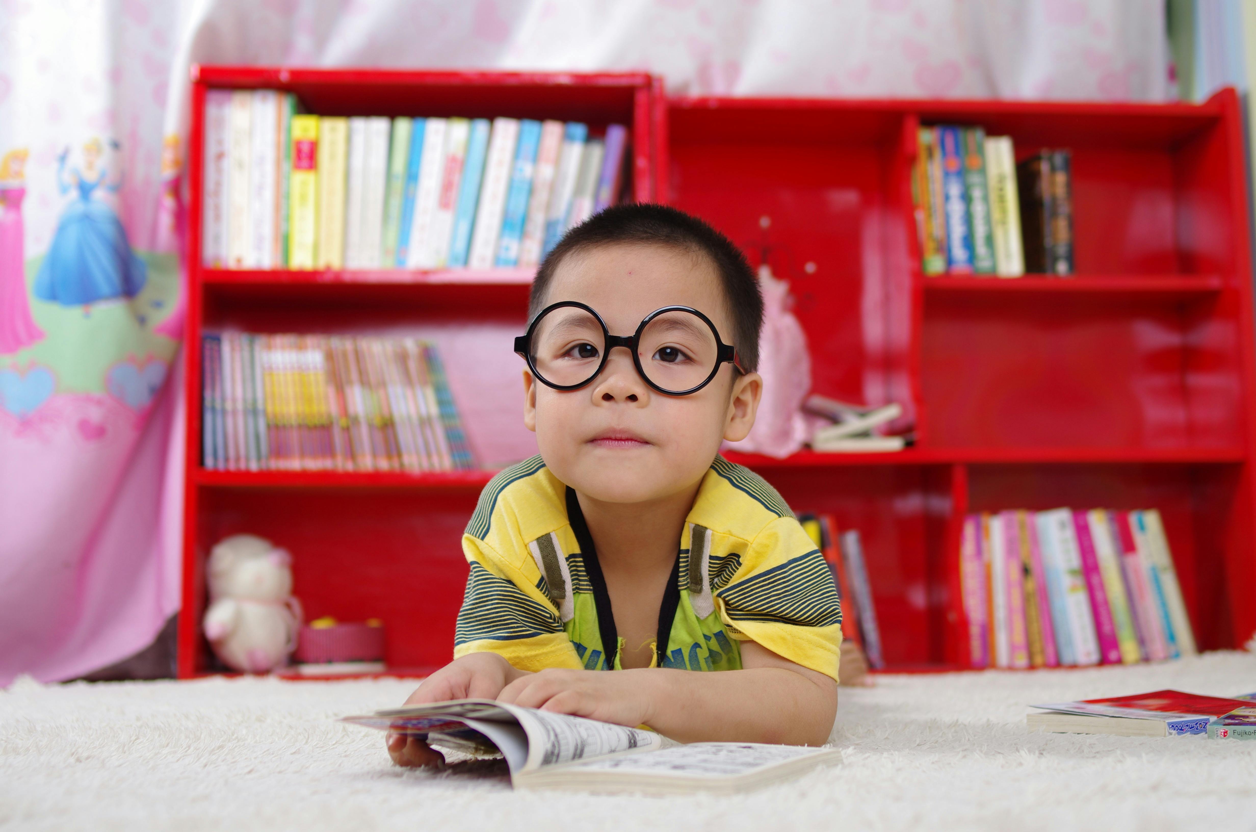 toddler wearing glasses laying on floor reading a book