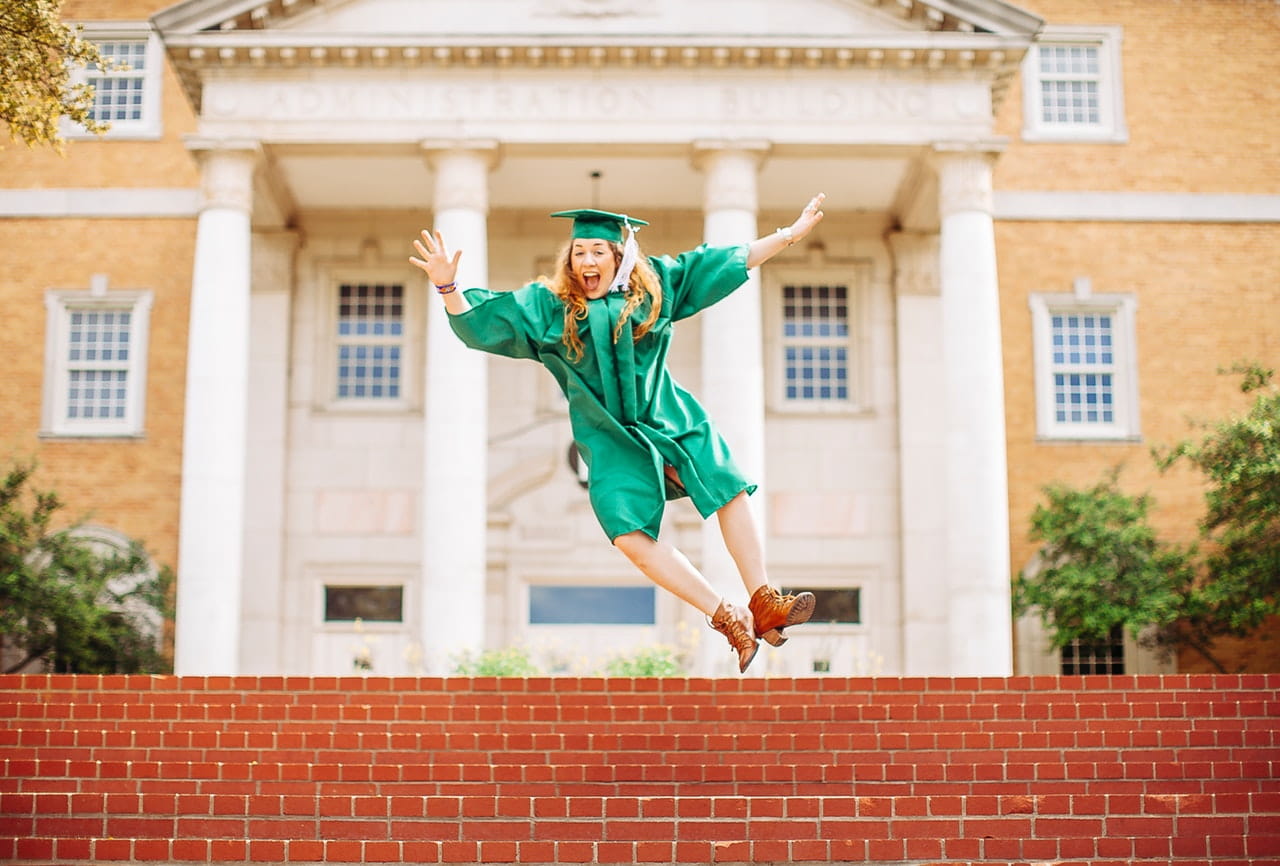 Woman jumping above stairs wearing graduation gown and hat