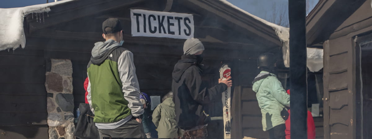 People standing in outdoor lines with ticket signage