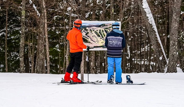 a skier and a snowboarder look at a trail map