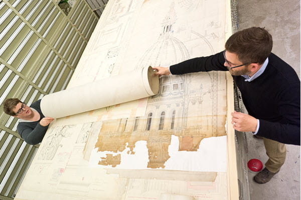 Two people unrolling a large historical map on a table.