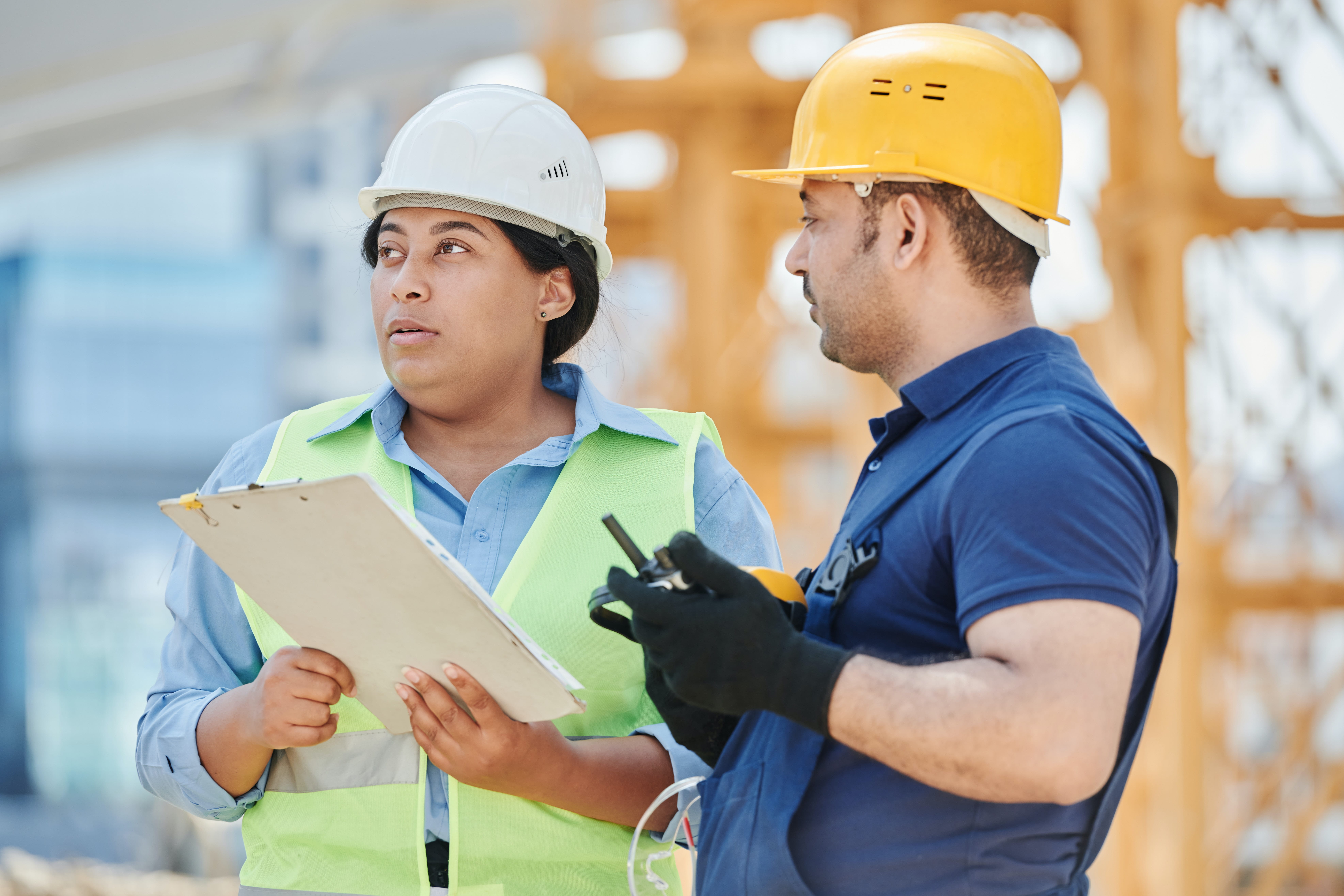 Photo of a man and women at a building worksite. The man is holding a radio and the woman a clipboard.