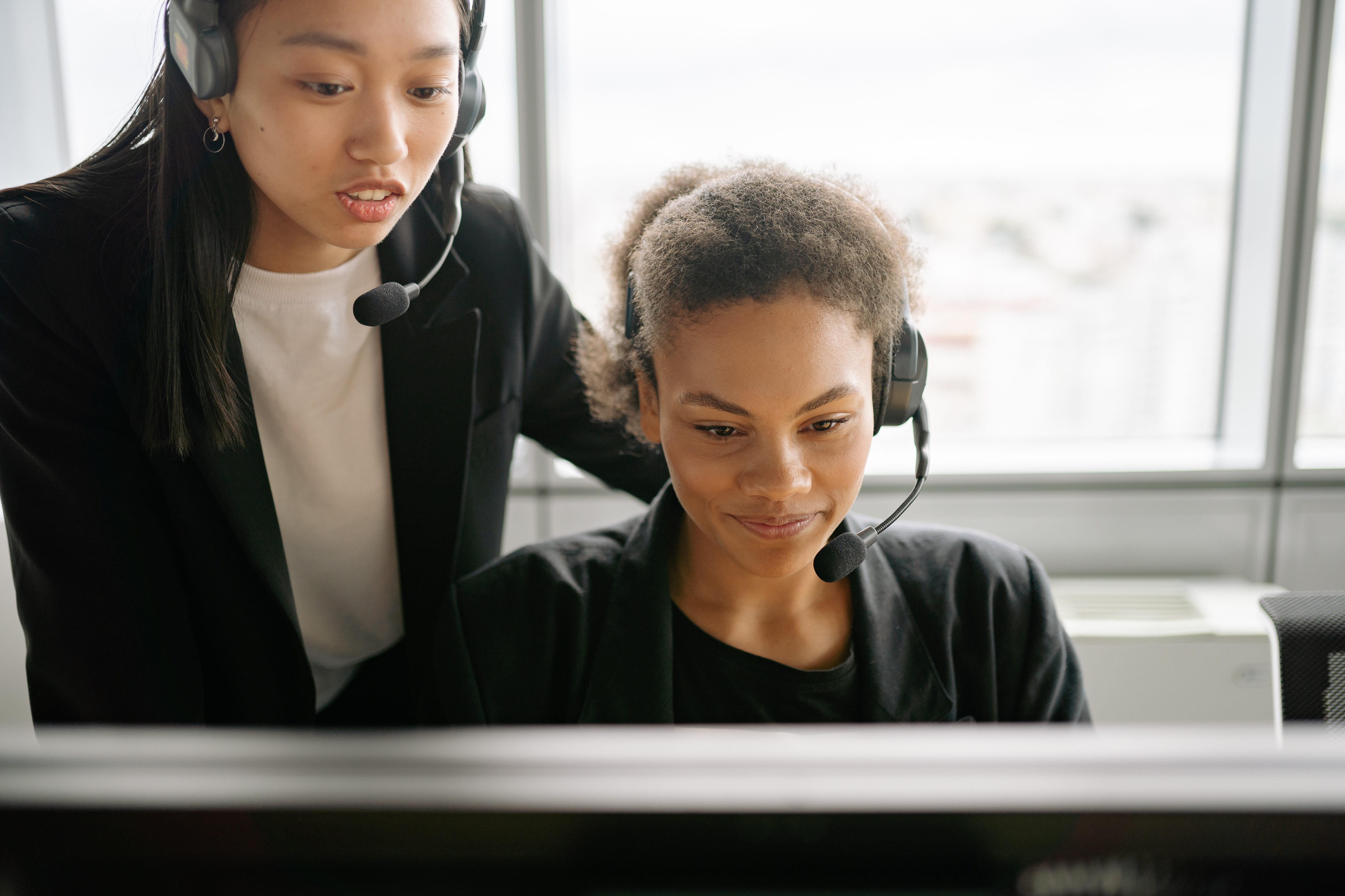 Two women with headsets on looking at a computer screen.