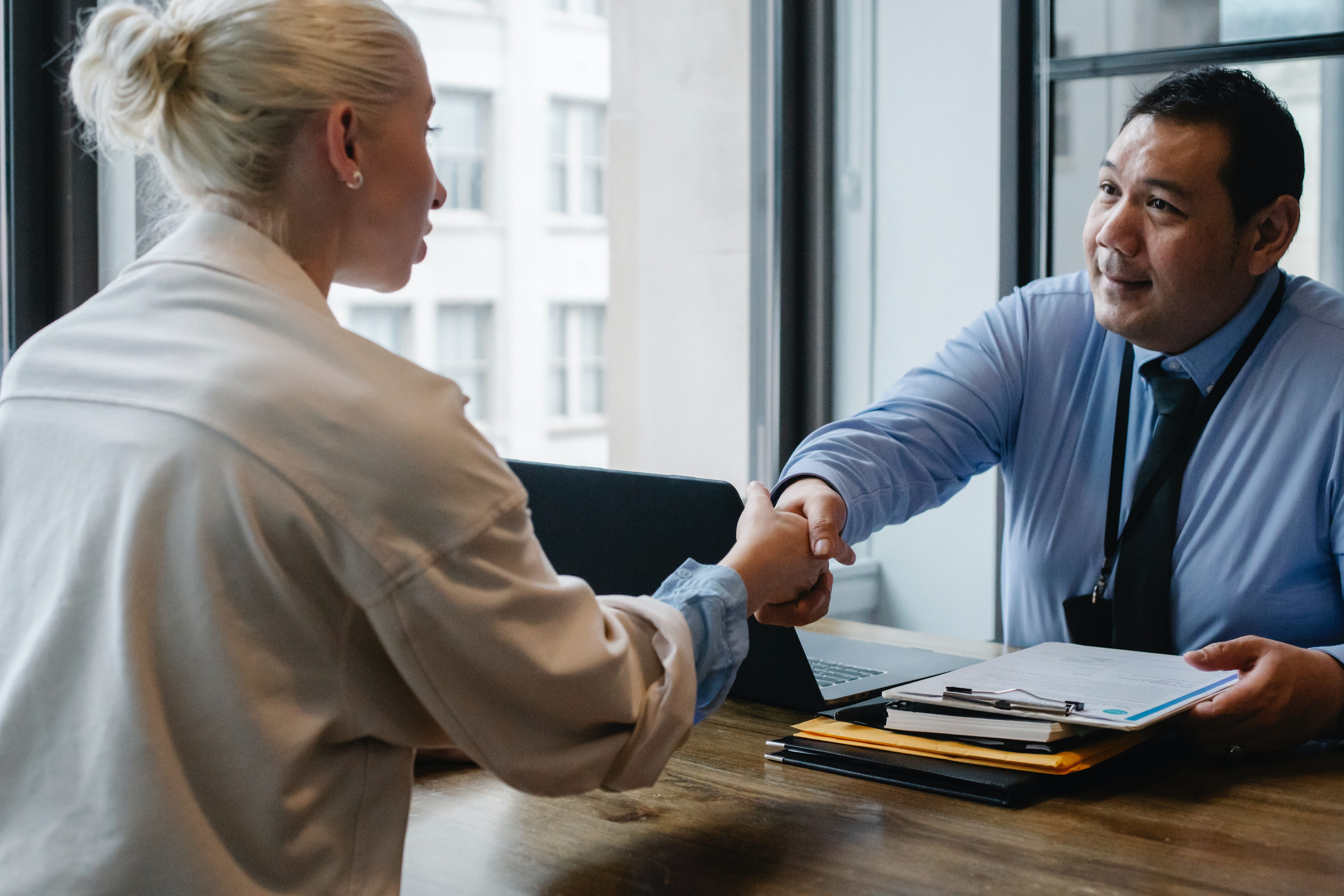Man shaking the hand of a woman. Both sitting at a desk.