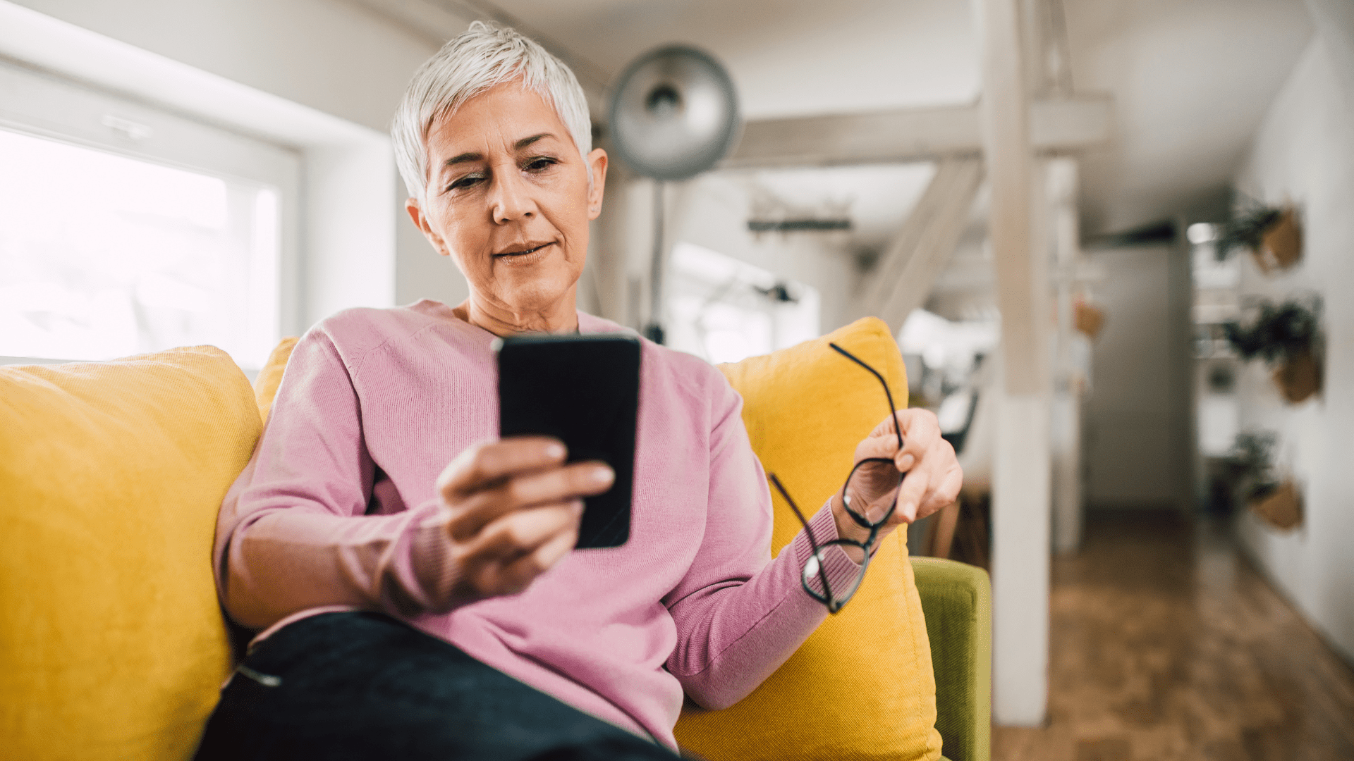Image of a older woman sitting on a couch looking at her phone.