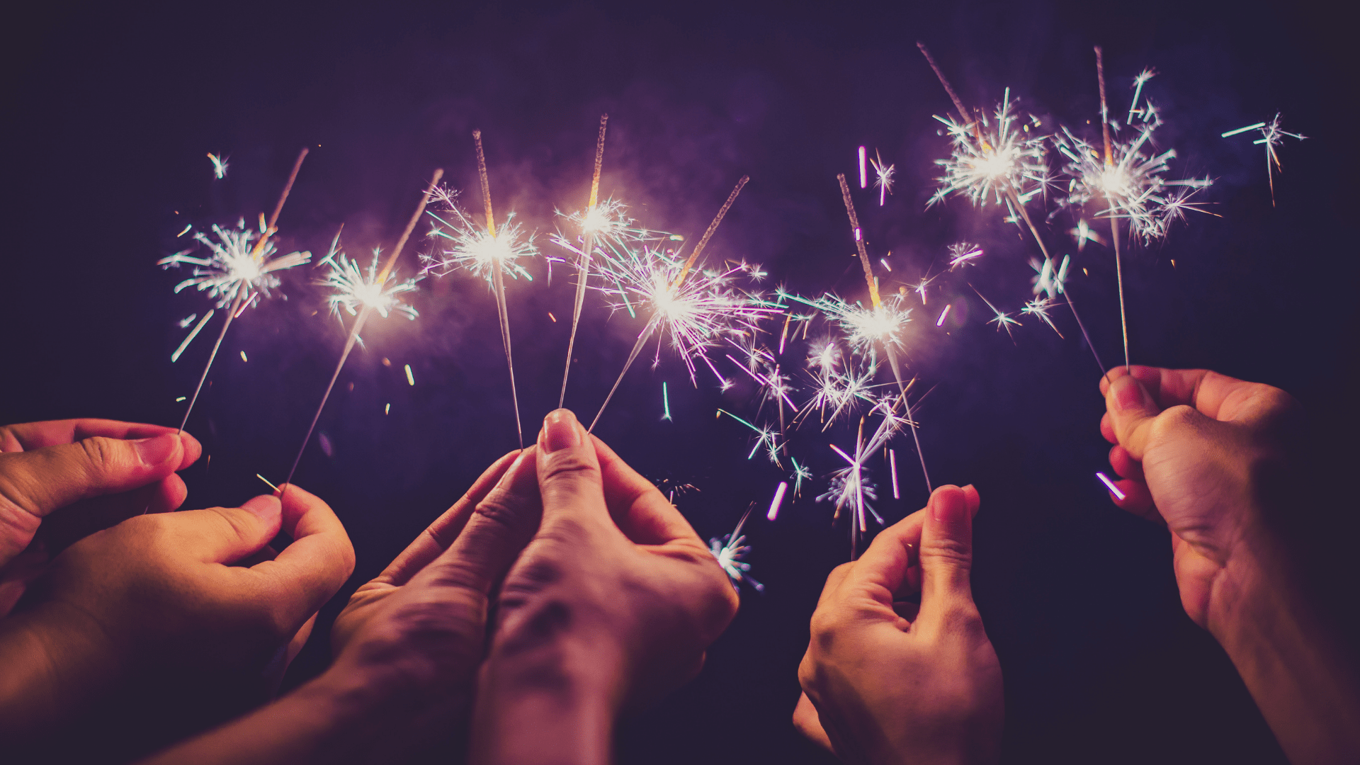 Photo of people holding lit sparklers at night.
