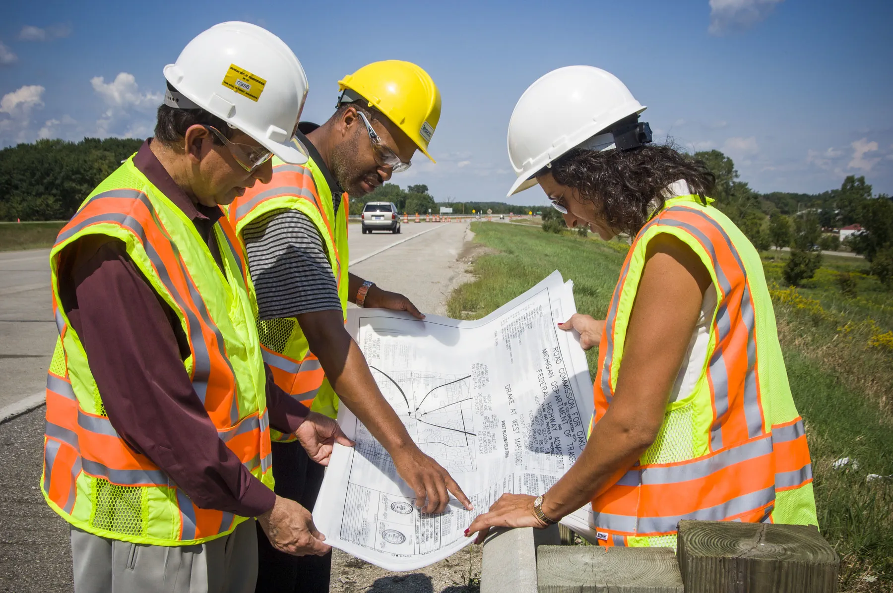 Photo of MDOT engineers in the field. Two men and a woman looking at road blueprints.