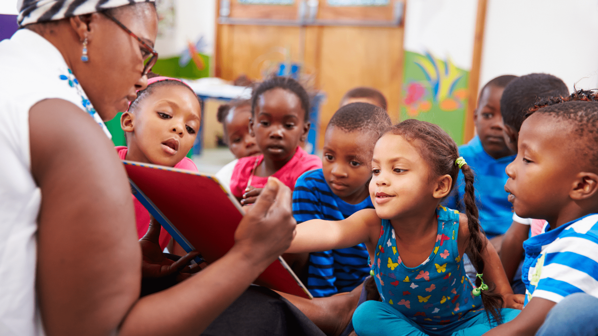 Photo of a woman teacher reading a book to several students.