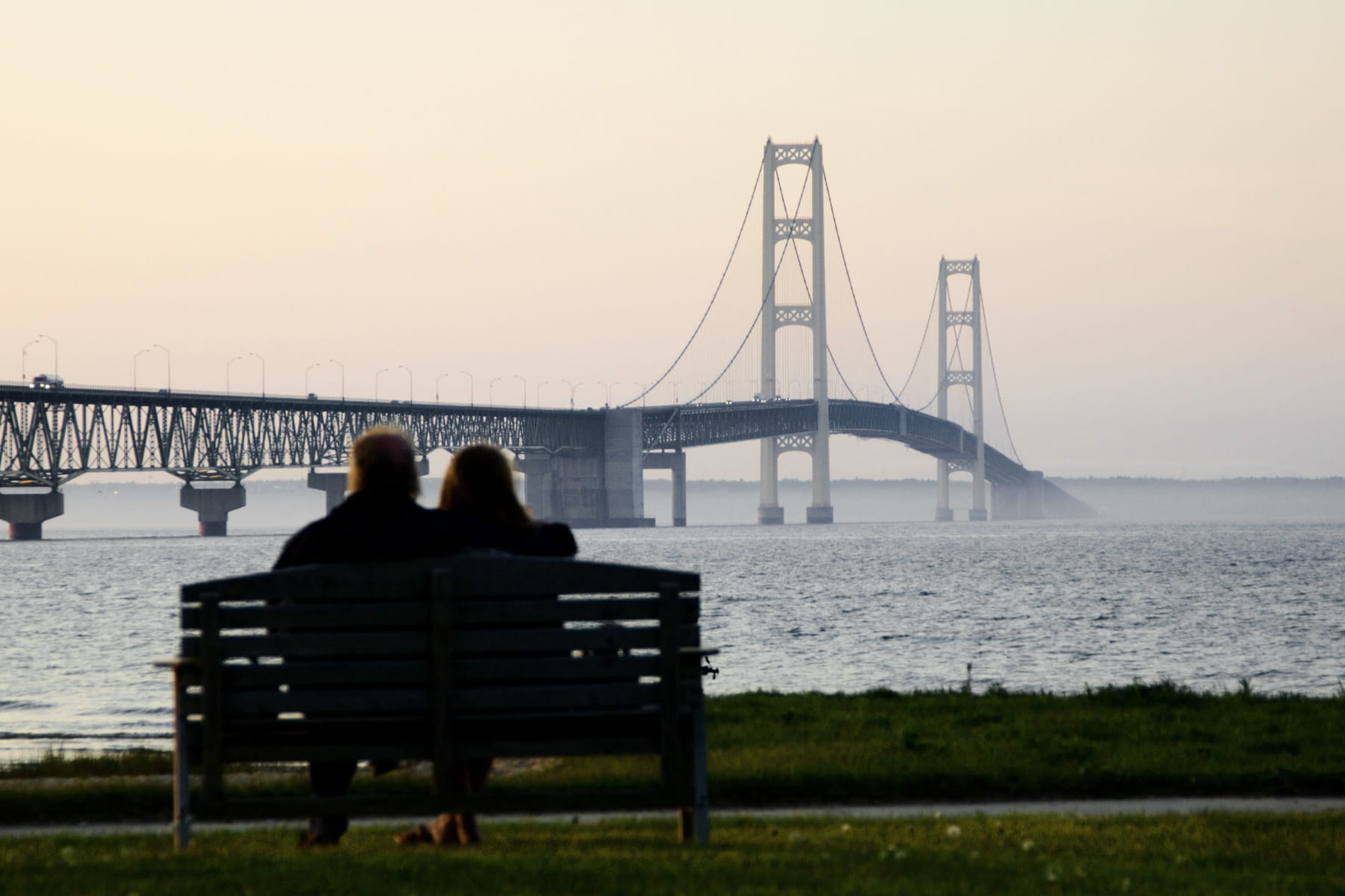 Two people sitting on a bench looking at a bridge.