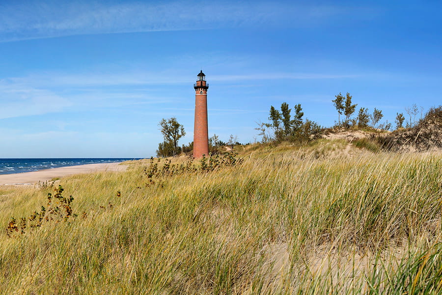 Photo of lighthouse with grass and water in the photo.