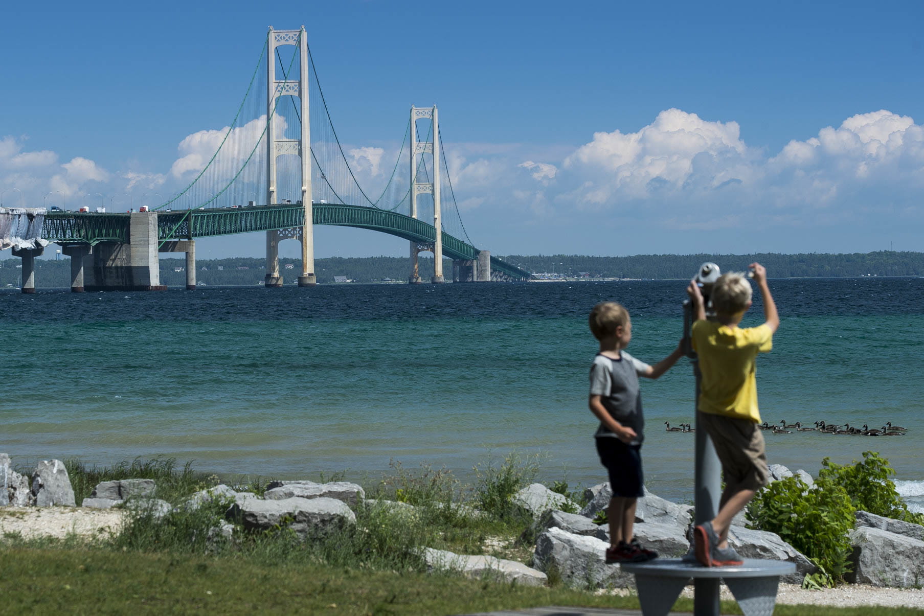 Two boys looking through a telescope at the Mackinac Bridge.