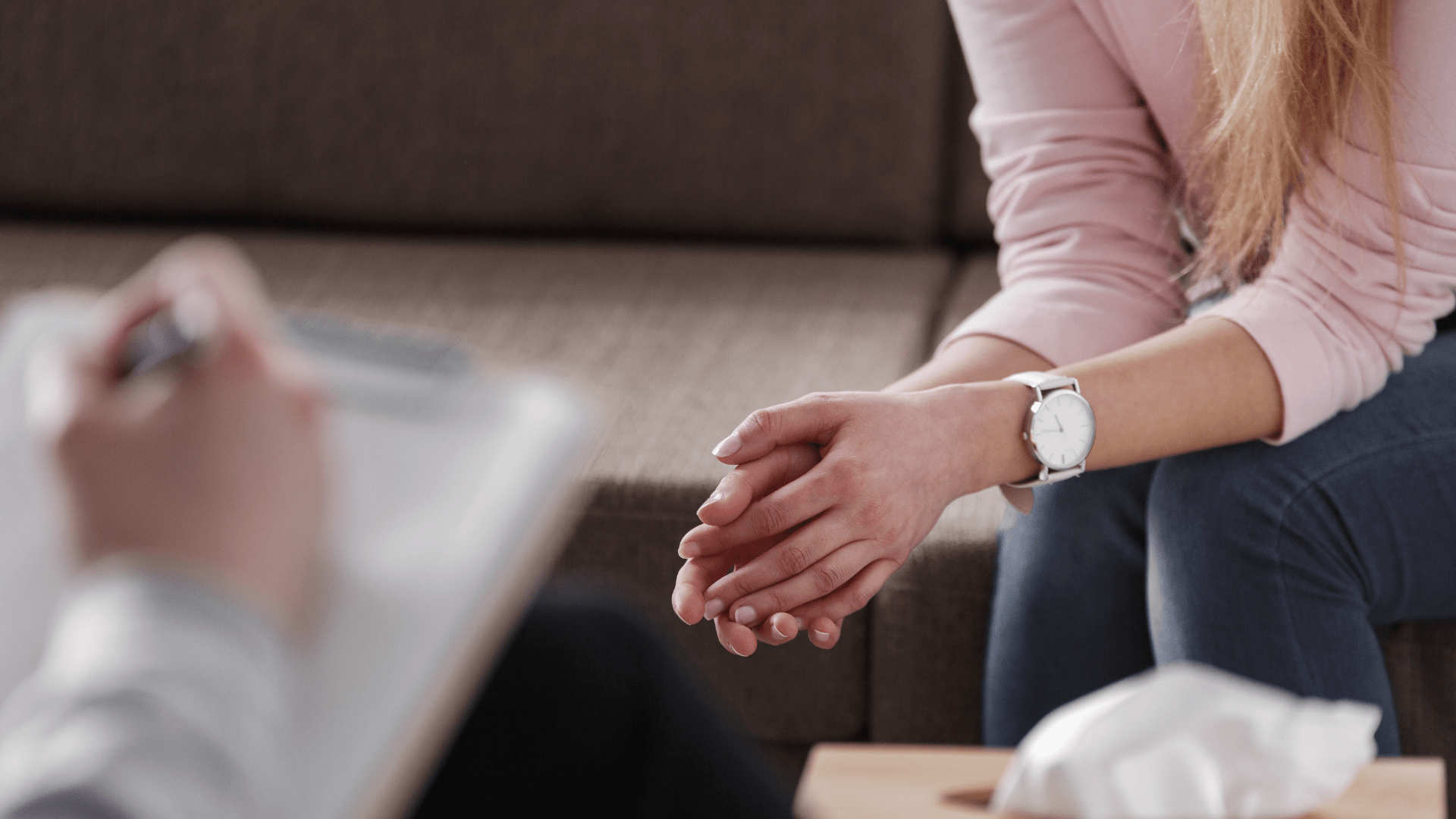 Image of a person sitting on a couch. Close up on their hands.