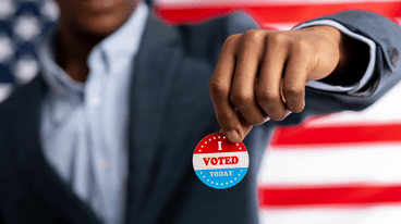 Person holding an "I voted" sticker in front of an American flag