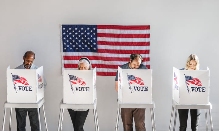 Four diverse voters standing behind voting booths with an American flag on the wall behind them