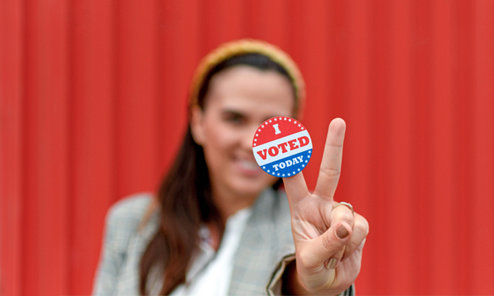 Young woman flashing a peace sign with an "I voted today" sticker on one finger