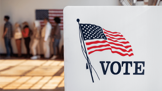 Up close of a voting booth with a line of voters in the background