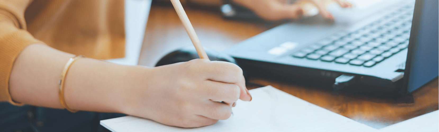 Someone writing on paper next to their computer.