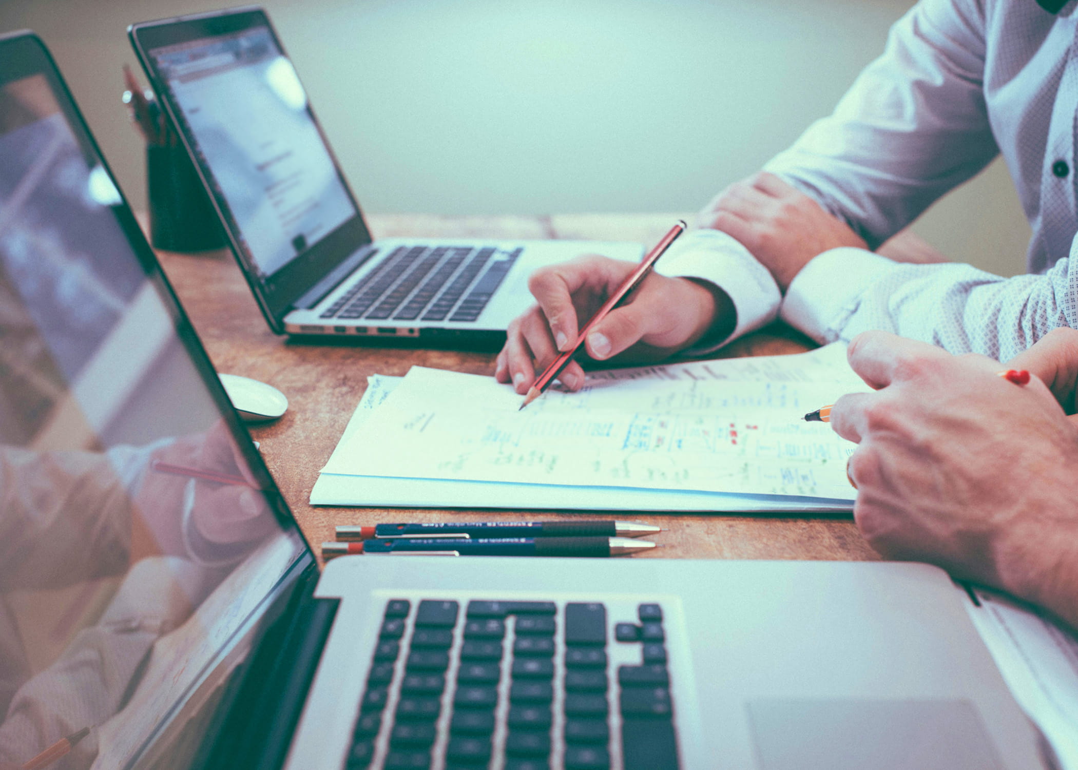 two people working on paperwork between two computers.
