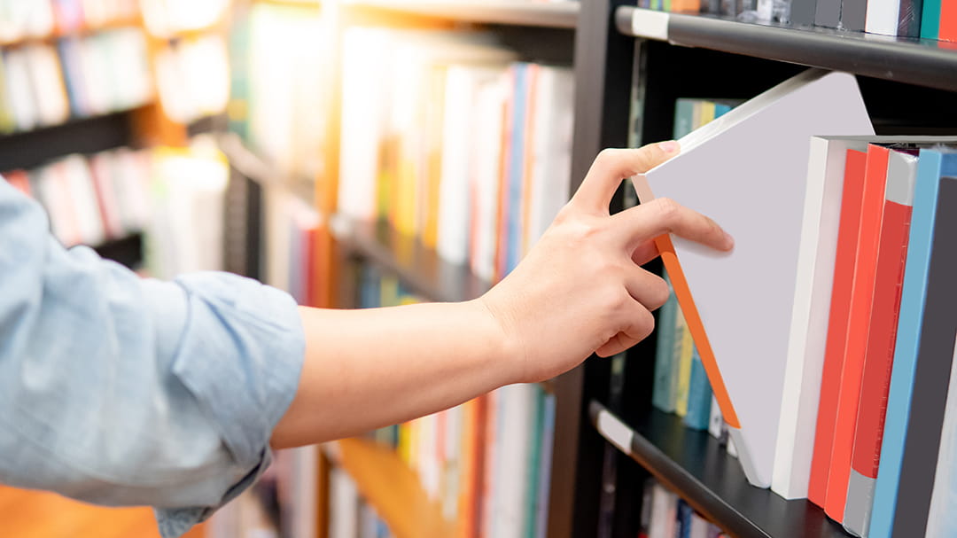 Hand pulling books from a bookshelf.