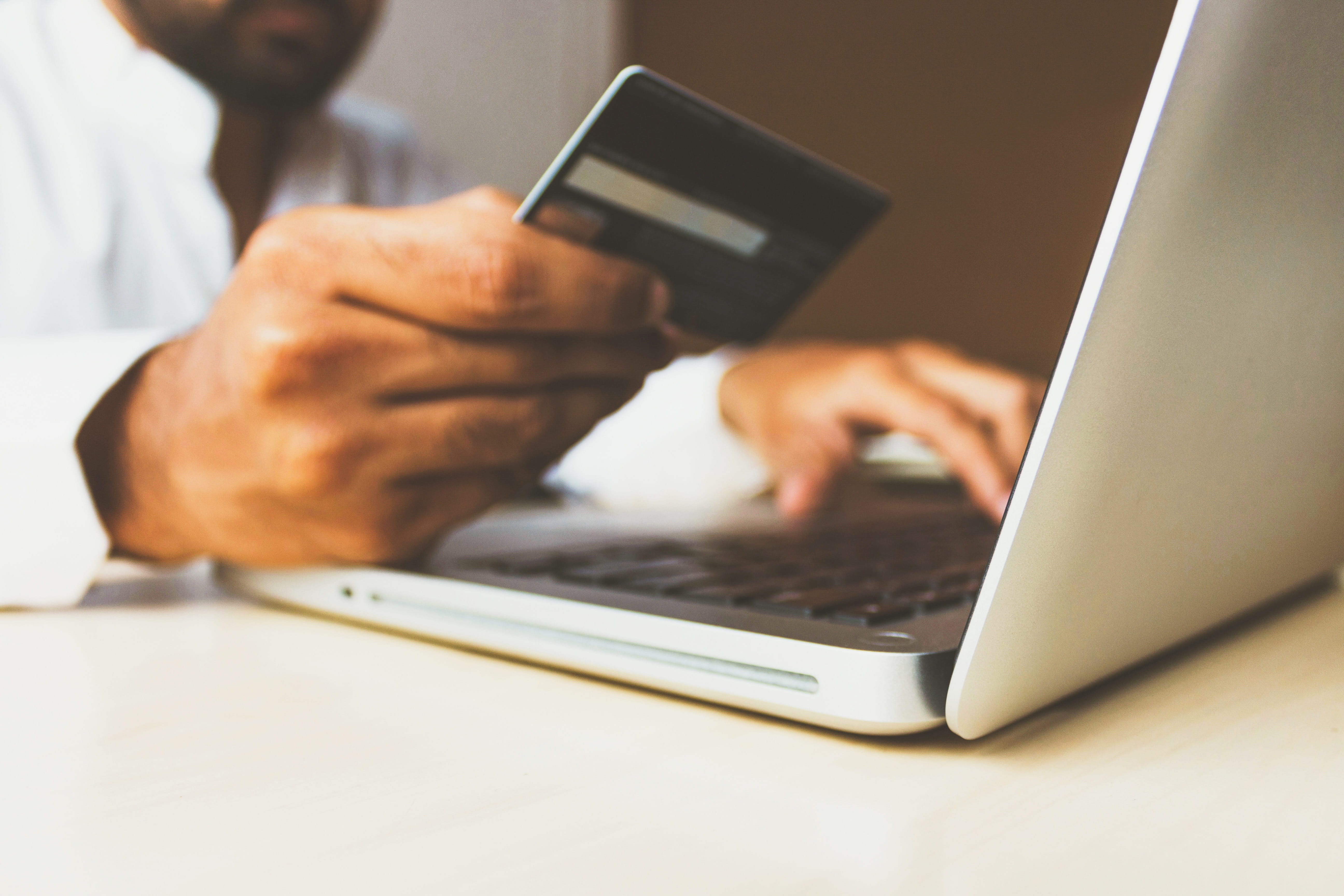 Hand holding a credit card in front of laptop computer.