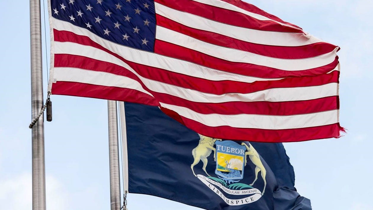Photo of US and Michigan flag flying in the wind.