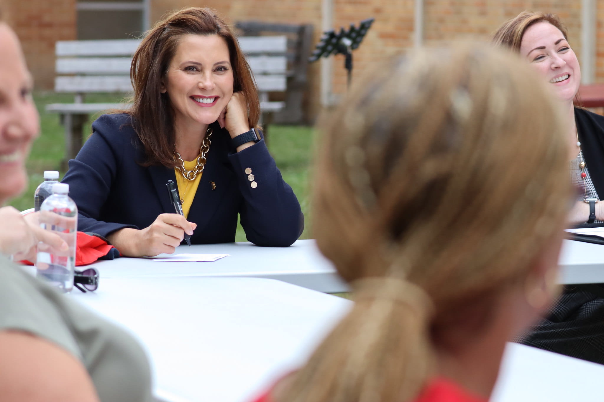 Photo of Governor Whitmer discussing key issues at a meeting with others. Sitting at a table outside. The Governor is smiling. 